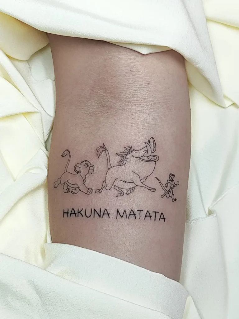 Tatuaje silueta Rey León con frase Hakuna Matata realizado en el brazo